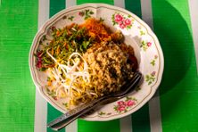 In this salad, rice gets topped with pinches of toasted coconut, dried fish, finely-sliced herbs and vegetables, bean sprouts, a tiny knot of noodles, crushed black pepper and dried chili. 